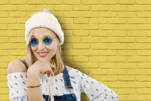 beautiful posing blond woman with winter hat, yellow wall background
