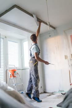 Construction worker wearing worker overall with wall plastering tools renovating apartment house. Plasterer renovating indoor walls and ceilings with float and plaster. Construction finishing works.