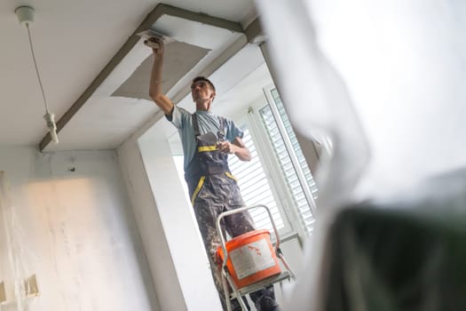 Construction worker wearing worker overall with wall plastering tools renovating apartment house. Plasterer renovating indoor walls and ceilings with float and plaster. Construction finishing works.
