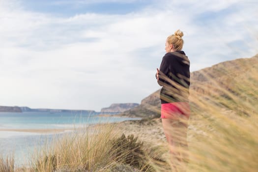 Woman, arms crossed, feeling chilled, enjoying last autumn sun, an beautiful Balos beach. Concept of vacations, freedom, happiness, enjoyment and well being.