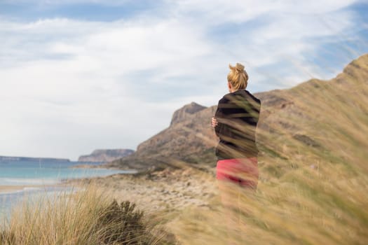Woman, arms crossed, feeling chilled, enjoying last autumn sun, an beautiful Balos beach. Concept of vacations, freedom, happiness, enjoyment and well being.