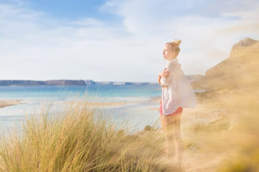 Woman, arms crossed, feeling chilled, enjoying last autumn sun, an beautiful Balos beach. Concept of vacations, freedom, happiness, enjoyment and well being.