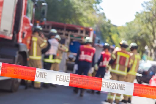Team of blured firefighters by firetruck on protected accident site. Focus on red and white security band.
