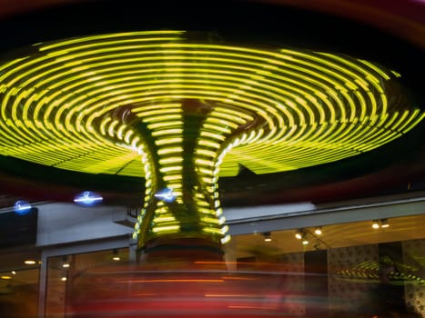 Flat-angled view of a kids funfair in motion at night with yellow stripes of light on a Christmas market.