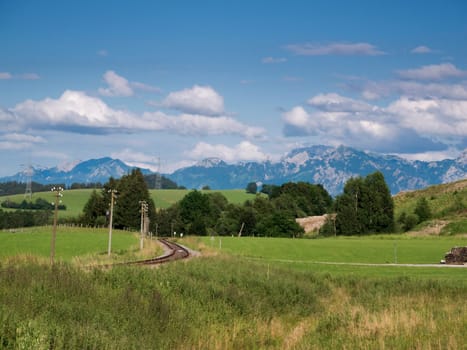 Landscape view in the Allgäu (Bavaria) with railway track,green meadow and blue sky with white clouds in summer.