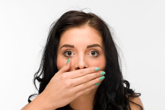 Frontal head view of a young black-haired woman against a white background vision frightens a hand holding in front of her mouth.