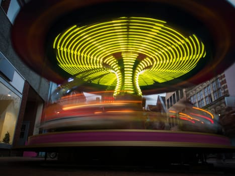 Flat-angled view of a children's carousel in motion at night with yellow light strips at a Christmas market.