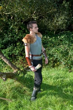 Medieval-dressed man stands in nature,holds drinking horn in his hand and looks to the right