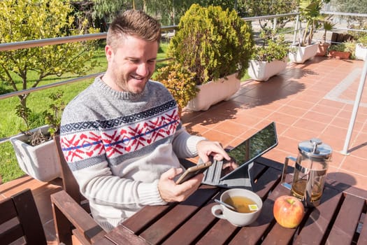 Happy man having breakfast with technology in the garden