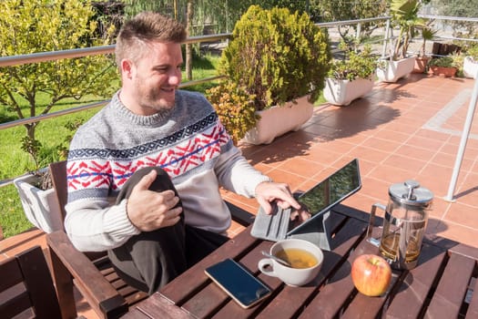 Happy man having breakfast with technology in the garden
