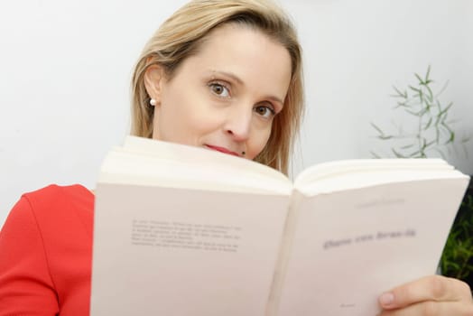 Beautiful blonde woman reads a book in the sofa at her home
