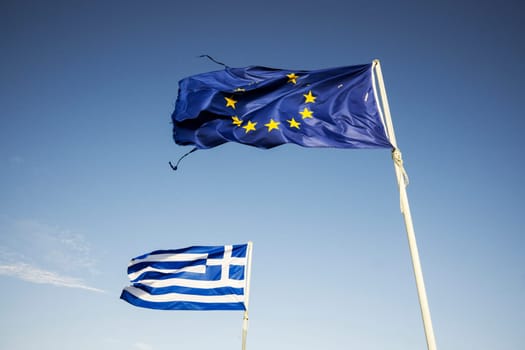 Ripped european Union flag and Greek flag, waving in the wind