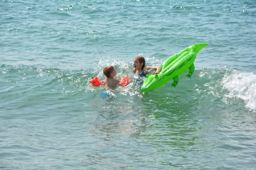 Two children swimming on a crocodile - air mattress in the sea waves