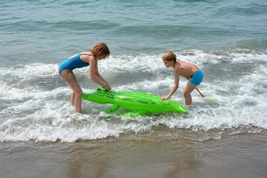 A boy and a girl playing on the sea beach with crocodile - air mattress
