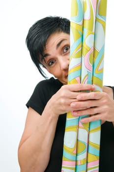 Upper body view of a middle-aged woman hiding behind wrapping paper rolls against a white background.