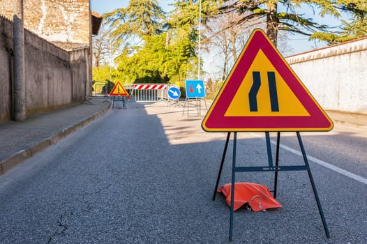 Road sign lane narrowing. In the background, blurred a roadworks site.