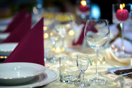 Beautiful plates and glasses on a table in a restaurant on the background of colored lights of candles