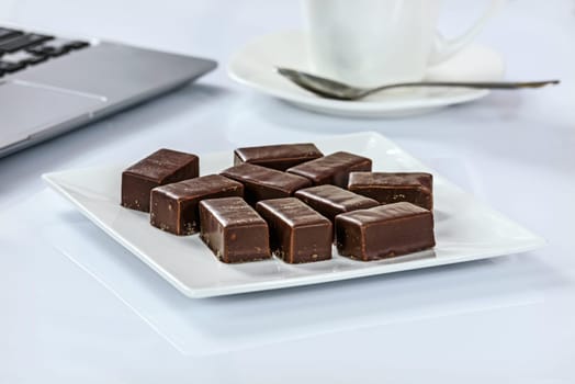 Chocolates on a plate next to a cup of coffee and laptop in the office