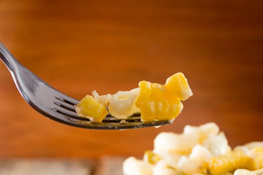 Close up of a fork and salad with pasta, yellow corn and Italian seasonings.