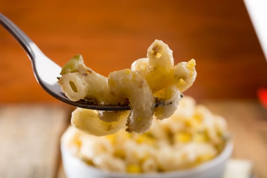 Close up of a fork and salad with pasta, yellow corn and Italian seasonings.