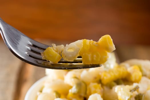 Close up of a fork and salad with pasta, yellow corn and Italian seasonings.