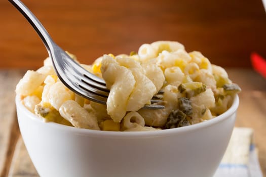 Close up of a fork and salad with pasta, yellow corn and Italian seasonings.