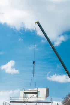 A wall part of a prefabricated house on a crane in front of a blue sky.