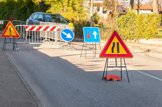 Road sign lane narrowing. In the background, blurred a roadworks site.