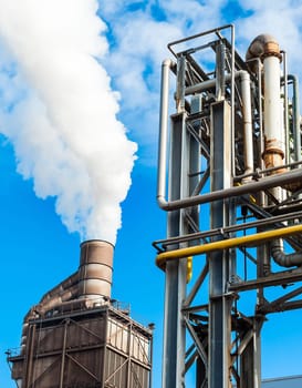 Pipes of chemical plant for factory, with smokestack on blue sky.