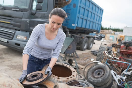 woman mechanic picking axle in car scrap yard