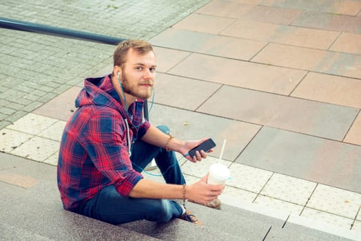 young man with soft drink sitting on stairs and using his smartphone