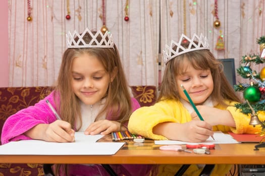 Two girls happily writing a letter to Santa Claus sitting at a desk in the home environment