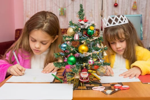 Two girls write a letter to Santa Claus, the focus is on the fur-tree in the middle