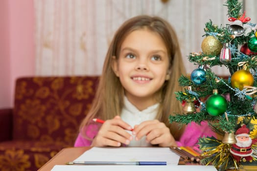 Happy little girl thinking of a gift for the new year, focusing on a fur-tree