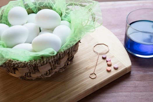 Easter eggs and glass container of blue dye with color tabs and egg dipping wire.