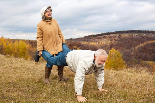 Elderly couple having fun and playing the wheelbarrow in nature.  "Woman carried his husband until old age."""