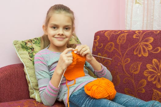 Girl sitting on the couch, knits on the needles, and looked into the frame