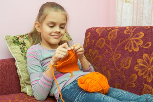 Girl lying on the couch and knits on spokes