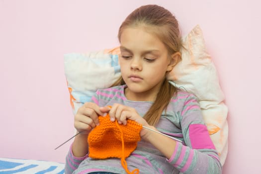 The girl knits on spokes sitting on the bed