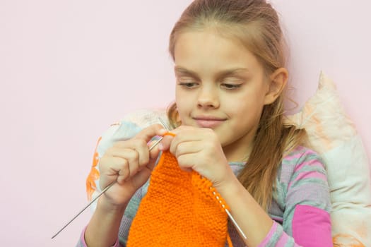 The girl knits on the needles orange scarf
