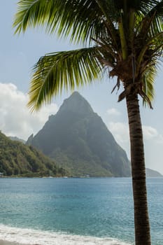 Beach view across the bay at Soufriere to the sea and Piton mountain. Framed with a palm tree