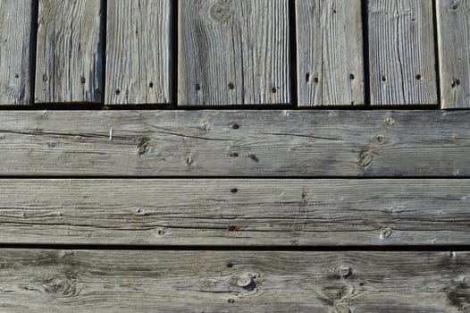 Silvery weather worn wooded planks on an old dock run both horizonally and vertically as a background with character