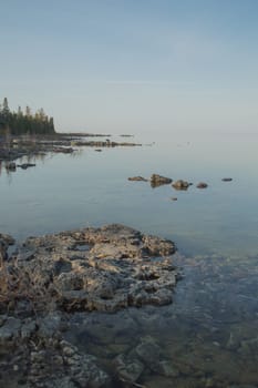 Dead calm afternoon image of clear lake huron water and limestone rocks along shoreline.