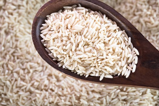 Wooden spoon full of brown rice.