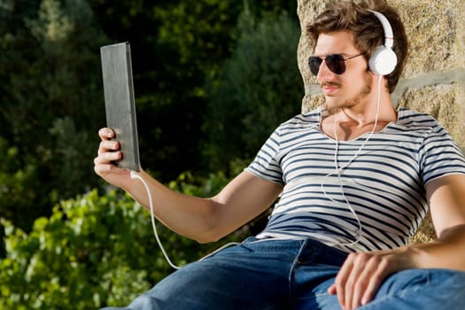casual man holding a tablet with headphones, outdoor