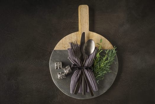 Christmas place setting with black silverware, fir greens and tiny gift parcels on wooden and slate board