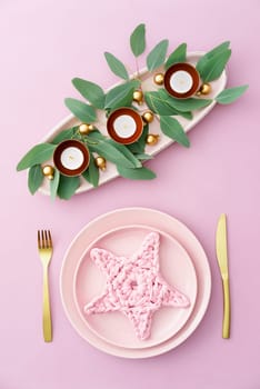 Christmas place setting in pink with golden silverware, eucalyptus and candles
