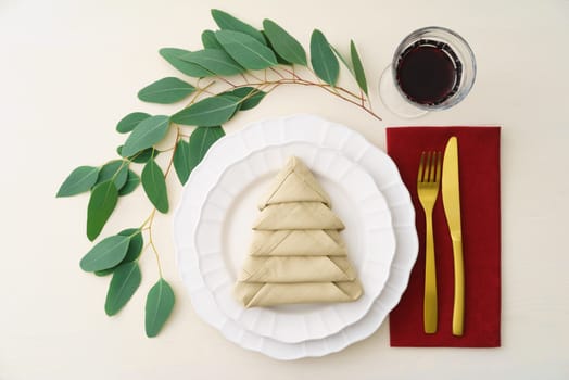 Christmas place setting with golden silverware, eucalyptus and a napkin folded as a Christmas tree