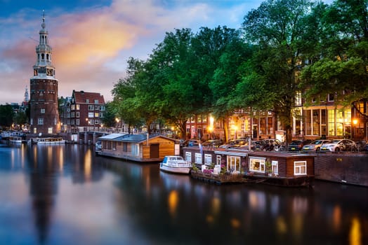Beautiful night in Amsterdam. Night illumination of buildings and boats near the water in the canal.