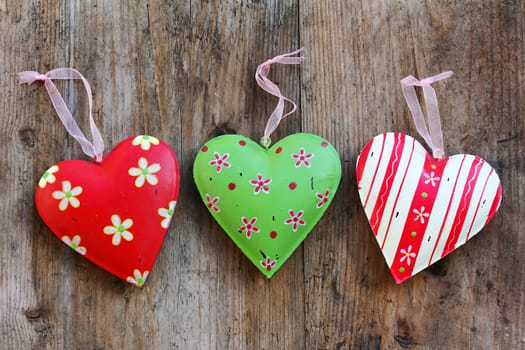 Three colorful metal hearts on a wooden substrate